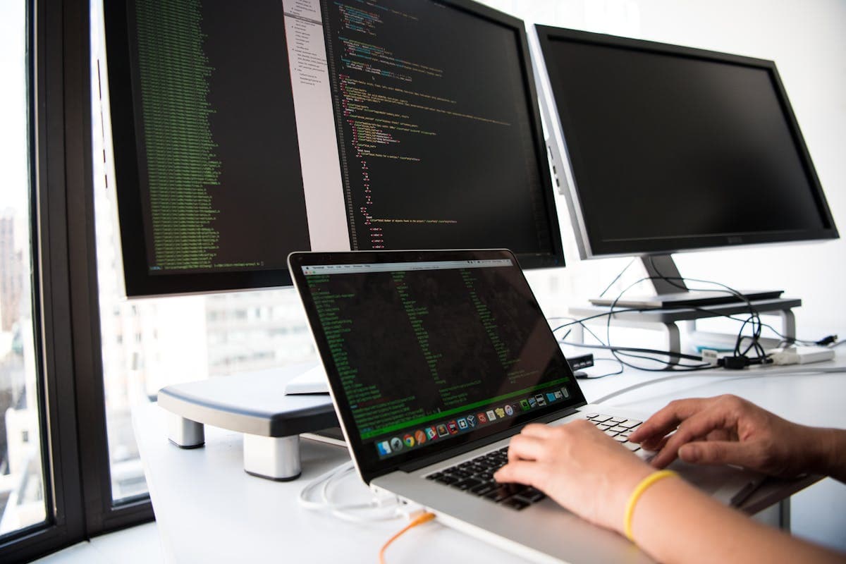 Person typing on a laptop with multiple monitors at a desk
